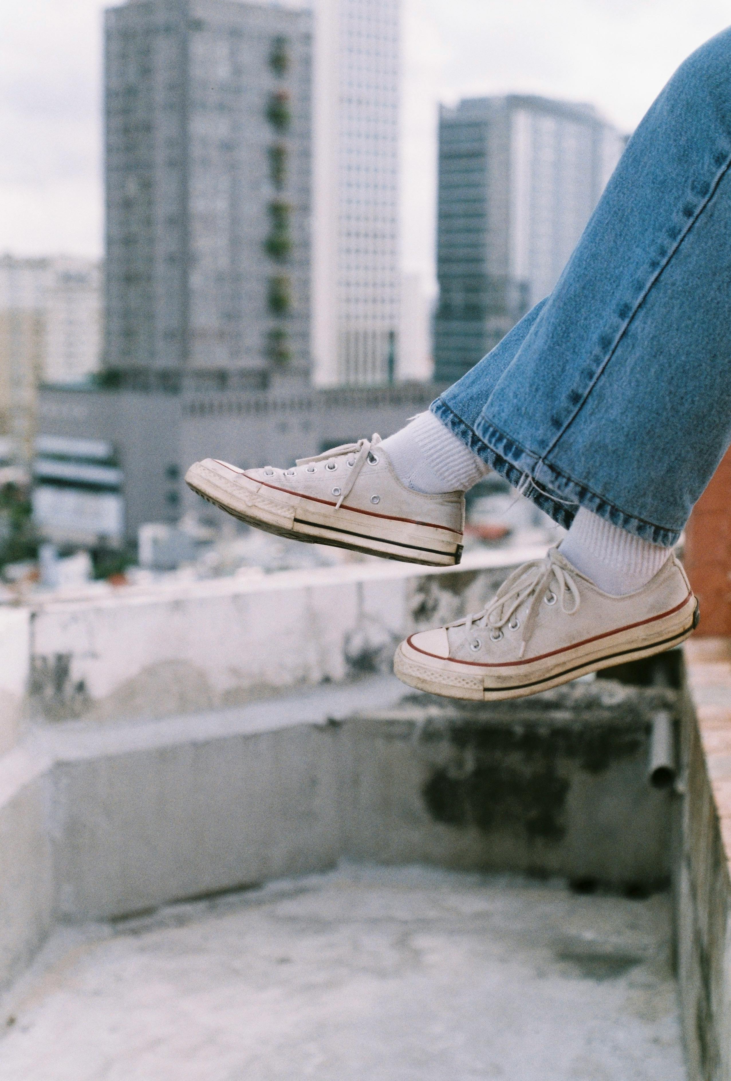 Casual sneakers dangling off a rooftop with city buildings in the background.