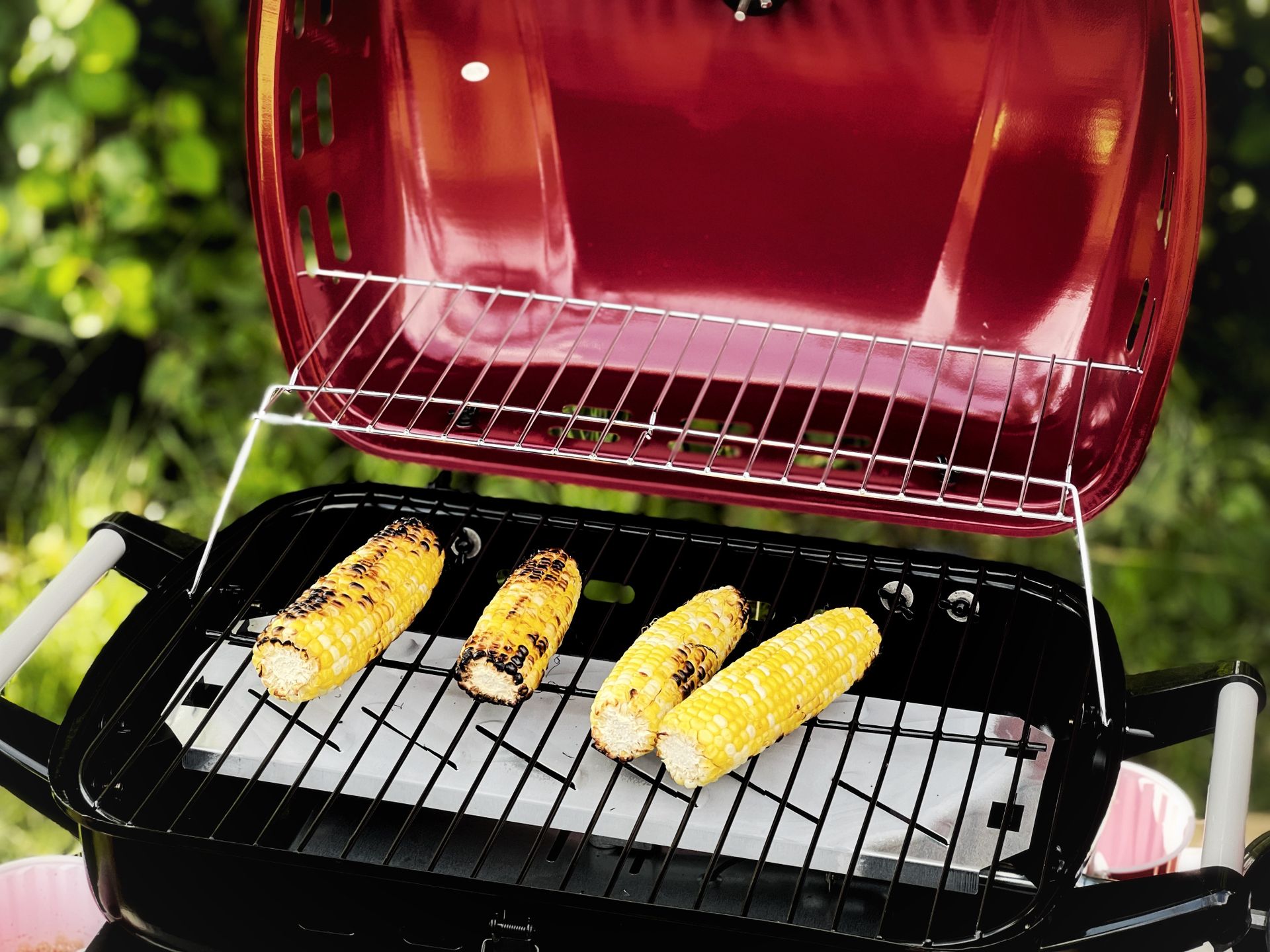 Four corncobs being grilled outdoors on a sunny day in a Canadian backyard.