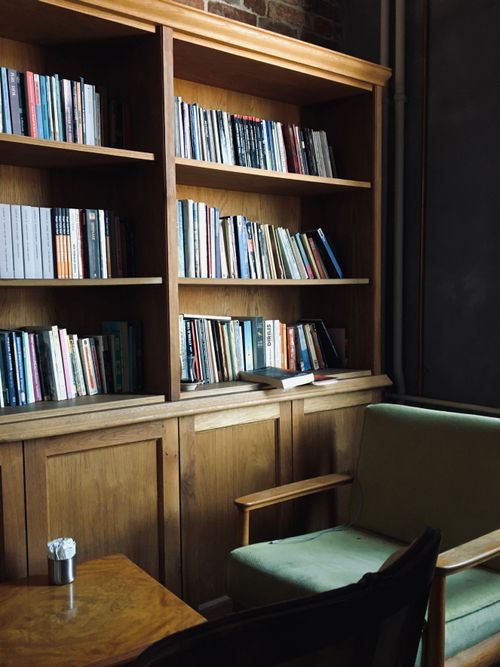 Free A cozy reading nook featuring wooden bookshelves filled with books and a comfortable chair. Stock Photo