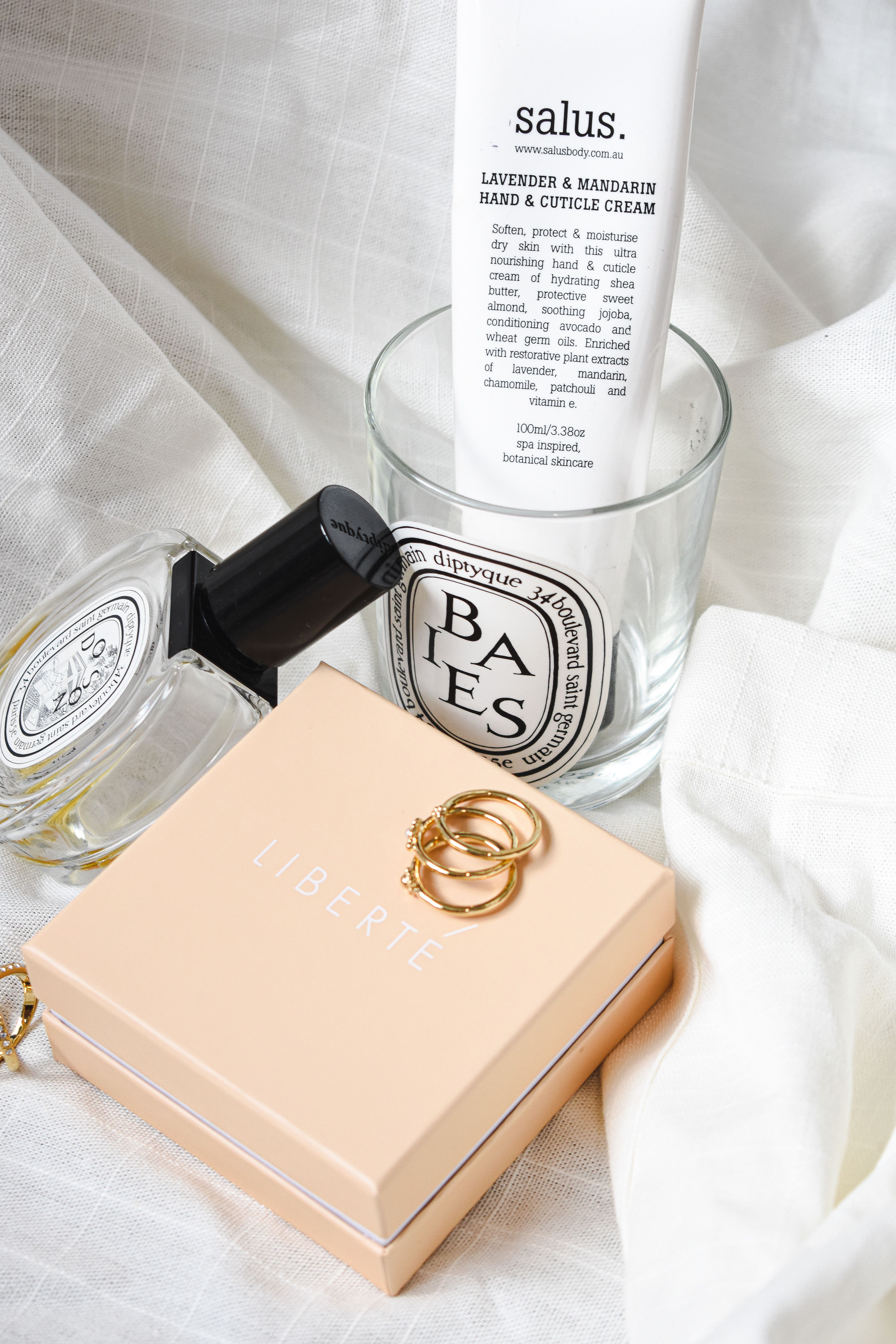Sophisticated arrangement of cosmetics, jewelry, and cream on white fabric, showcasing elegance and style.