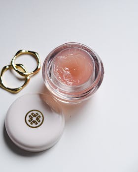 A pastel pink cosmetic jar with a lid and gold rings on a white background. Ideal for skincare branding.