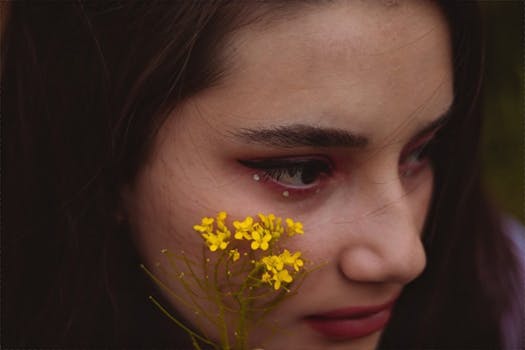 A thoughtful close-up portrait of a woman with yellow flowers touching her face.
