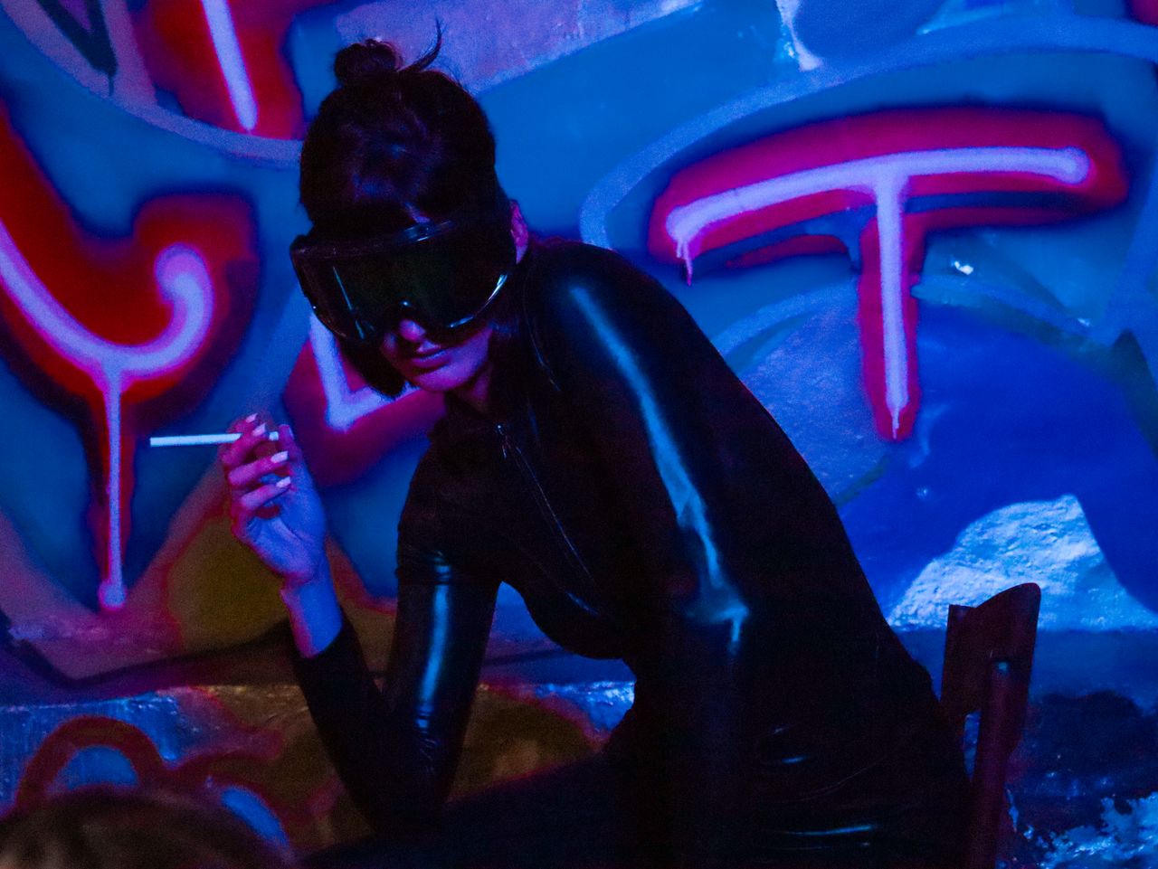 stylish woman in a dark outfit with sunglasses posing against vibrant