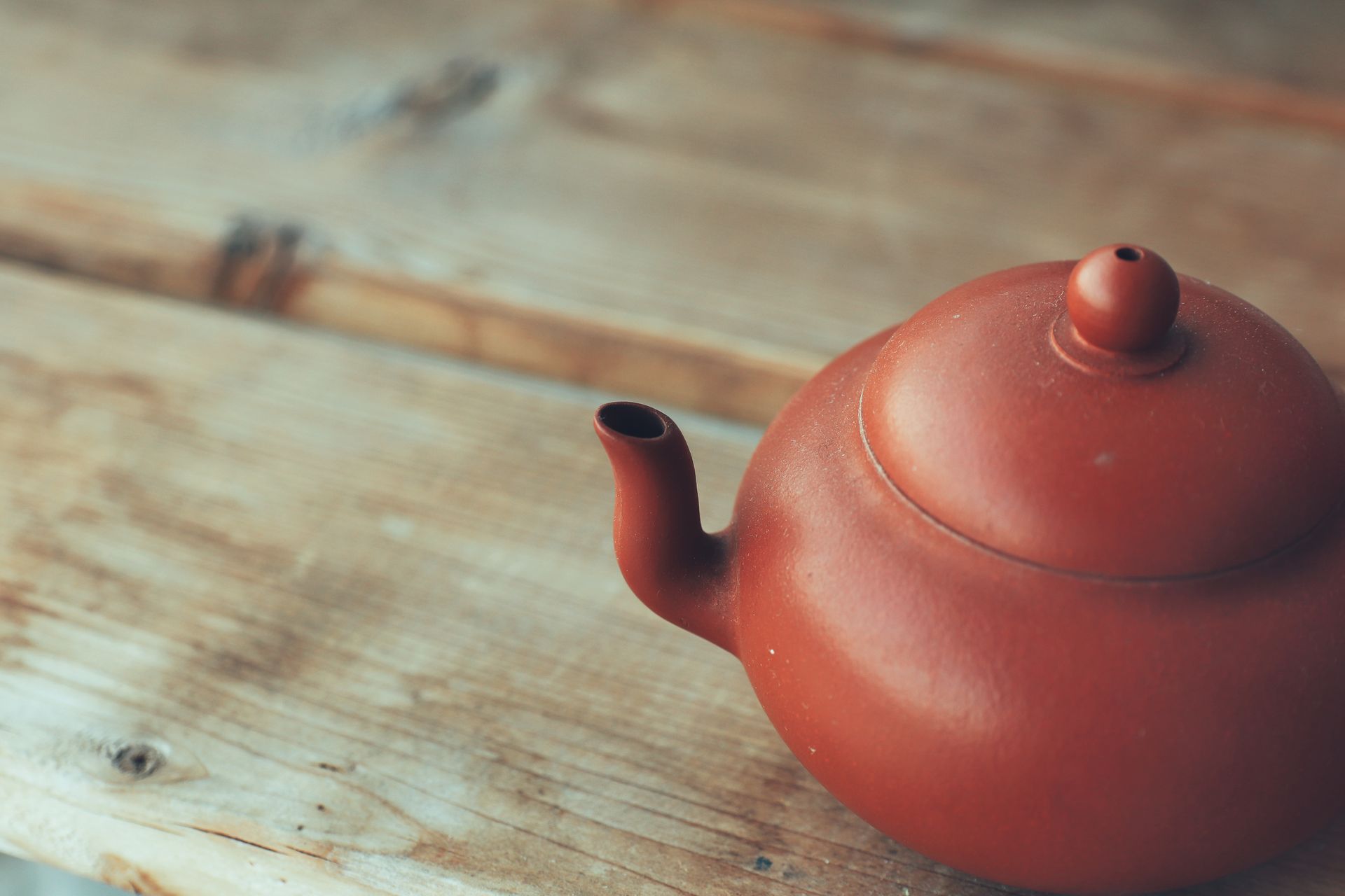 A close-up of a red clay teapot placed on a rustic wooden table with soft lighting.