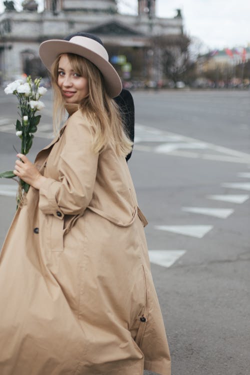 A Woman in Brown Coat Holding White Flowers