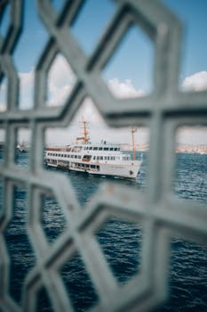A ferry travels across the Bosphorus in Istanbul, seen through a geometric frame against a blue sky.