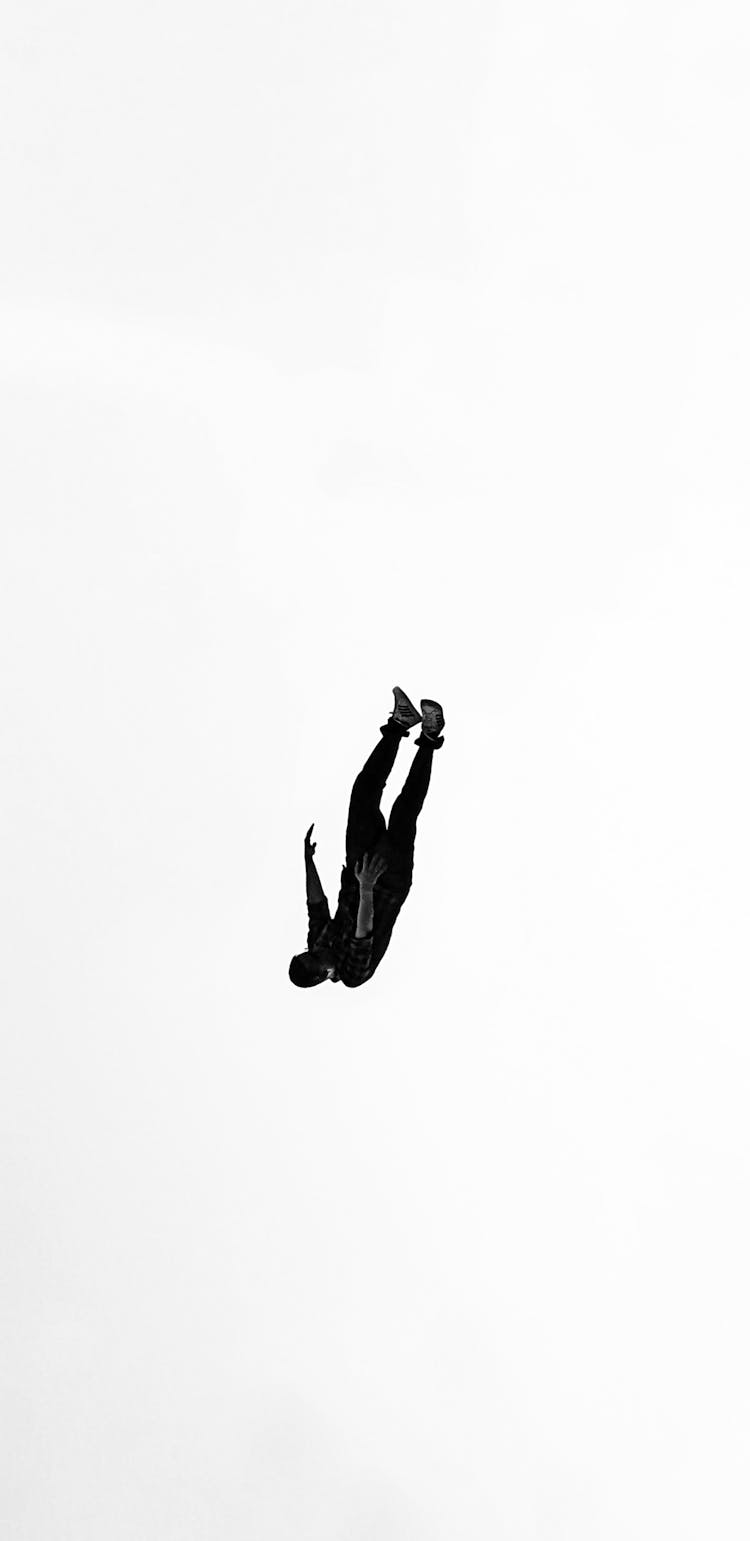 Silhouette Of A Man Falling Down Against White Background