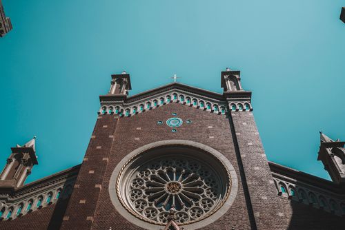 Free Low-angle view of an ornate brick church facade with blue sky background. Stock Photo