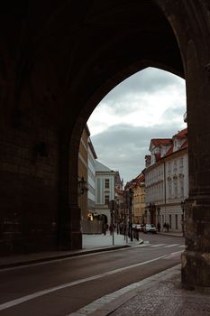 View through archway to a historic city street, featuring ornate architecture and moody atmosphere.