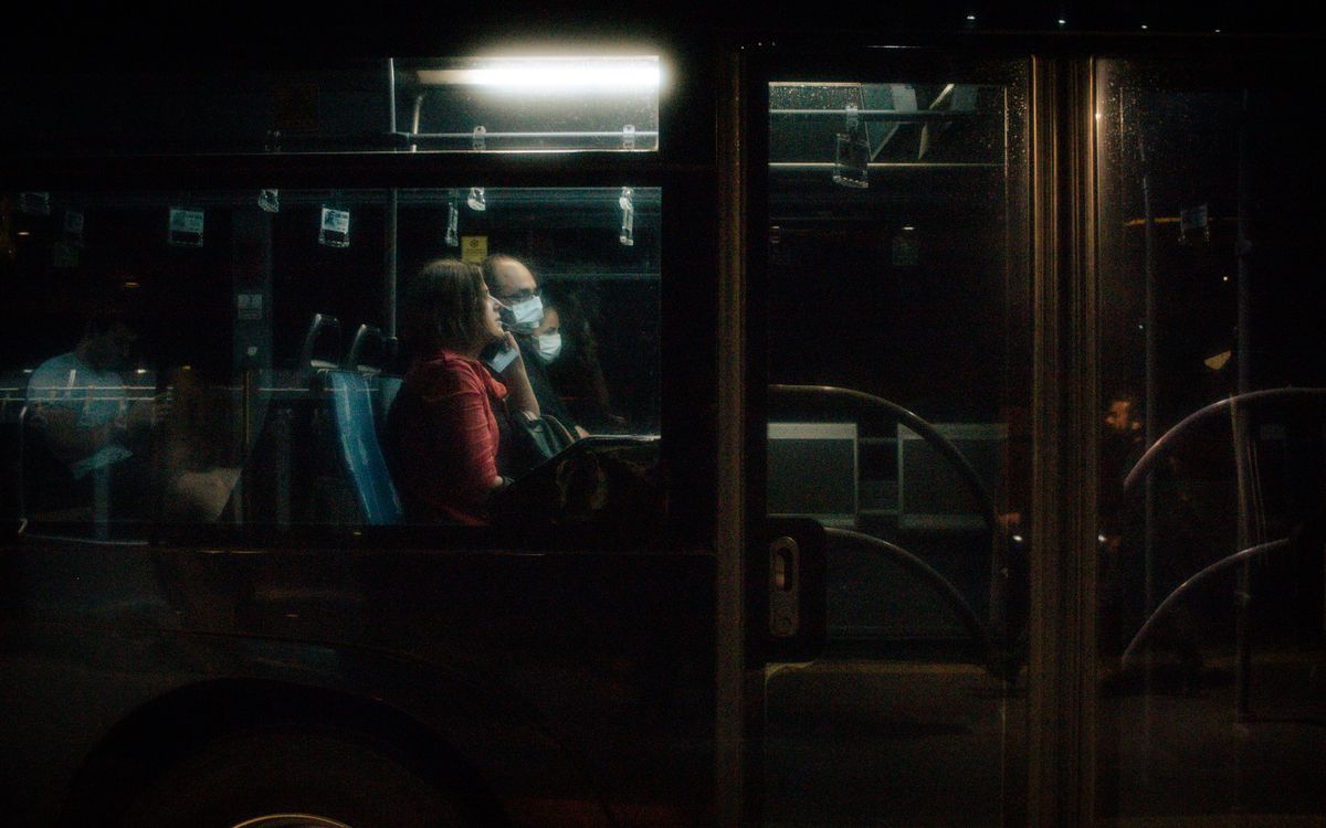 Passengers wearing masks commute on a city bus at night, reflecting pandemic life.