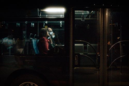 Free Passengers wearing masks commute on a city bus at night, reflecting pandemic life. Stock Photo