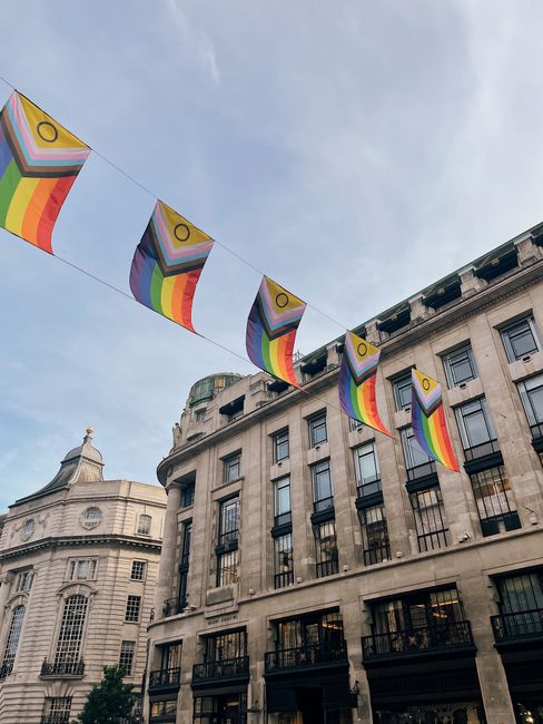 Triangular pride flags hanging above buildings against a blue sky in urban environment.