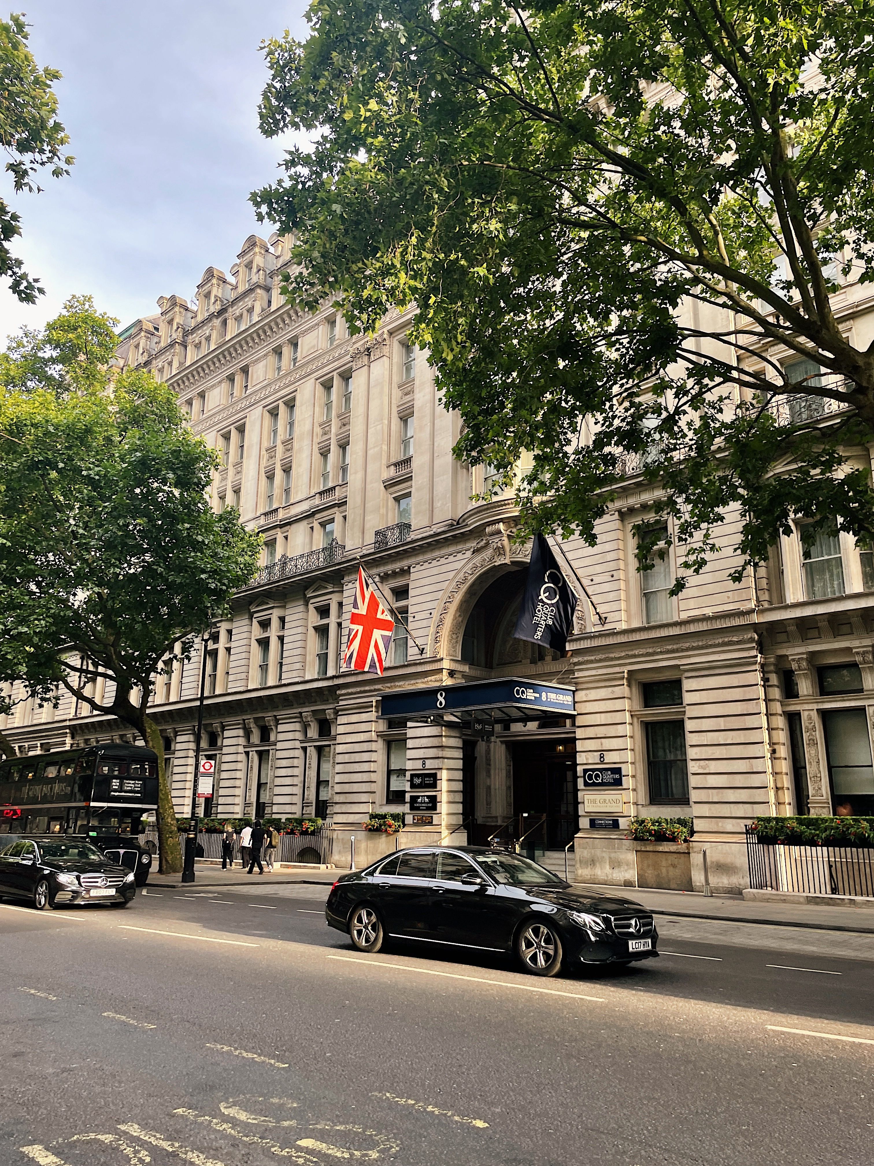 Classic London street with historical architecture, cars, and flags.