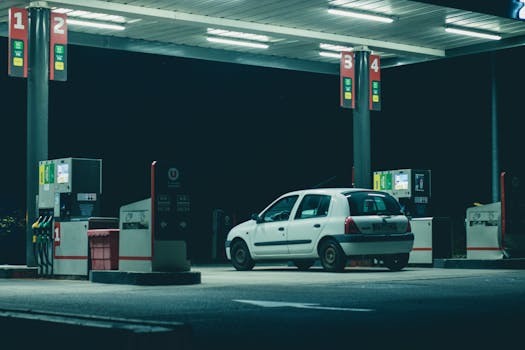 A solitary white car parked at a gas station under bright lights in a nighttime setting.