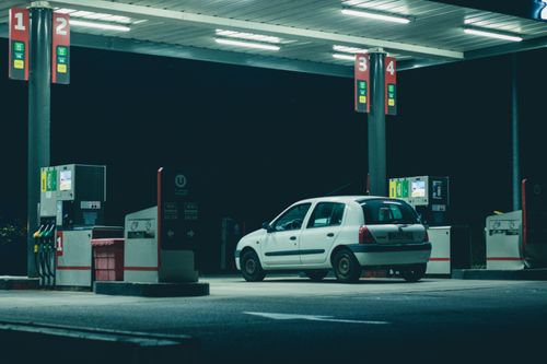 Free A solitary white car parked at a gas station under bright lights in a nighttime setting. Stock Photo