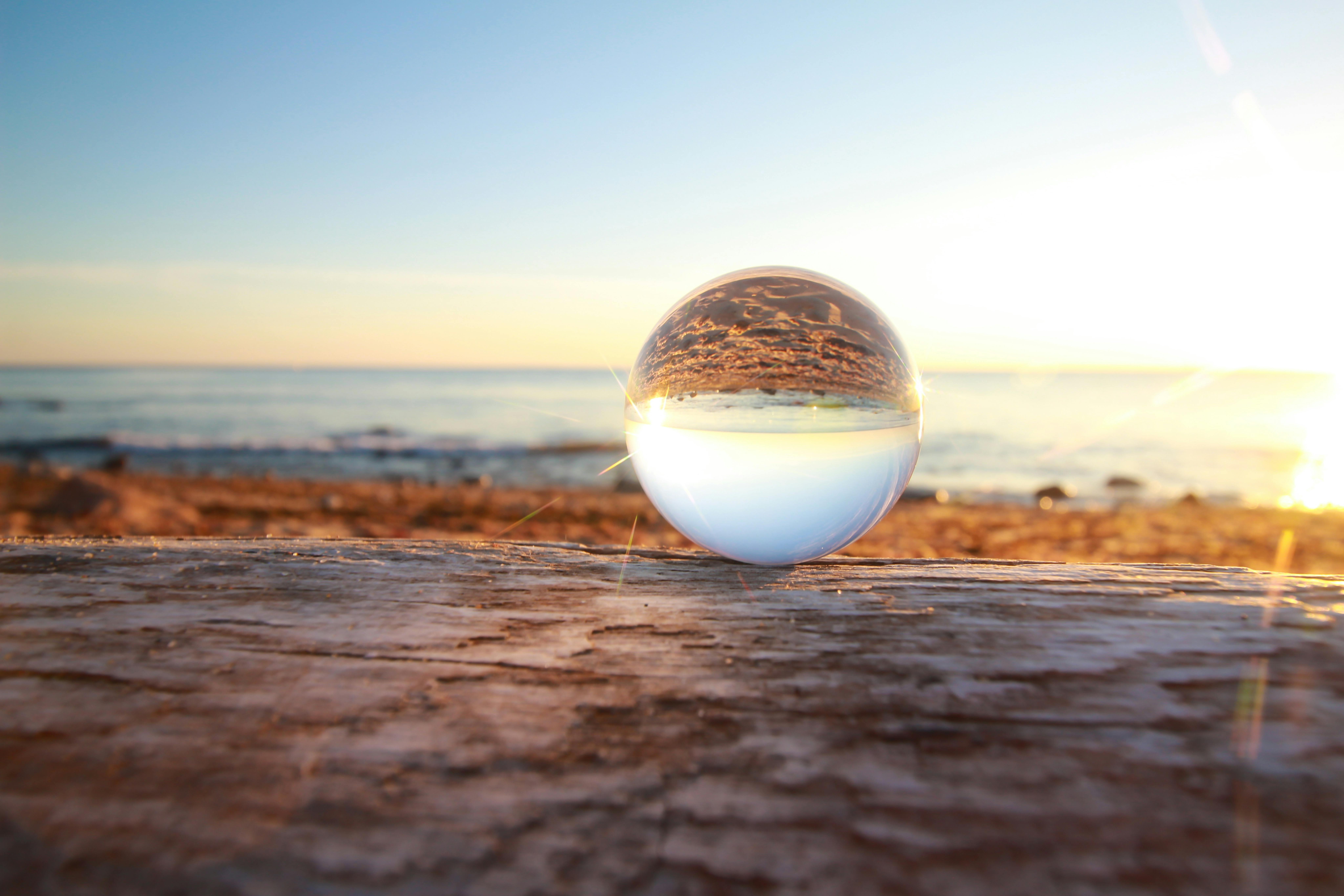 Clear Marble Toy Reflecting Seashore during Golden Hour