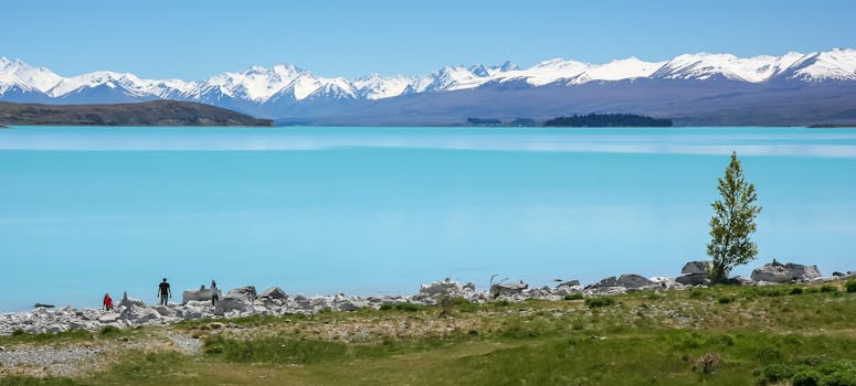A tranquil turquoise lake with snow-capped mountains and a scenic shoreline under a clear sky.