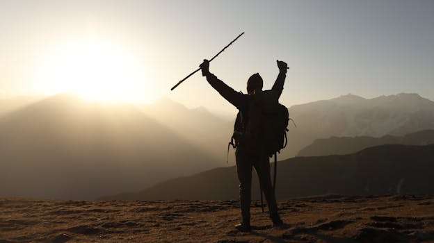 A lone backpacker raises arms triumphantly at sunrise on a mountain peak.