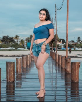 Adult woman in casual wear standing on a dock at the beach with a scenic ocean backdrop.