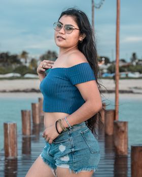 A young woman in an off-shoulder top enjoying a summer day on a wooden dock by the ocean.