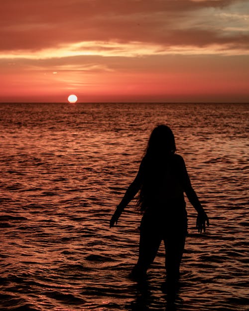 Silhouette of a Woman Standing on the Beach during Sunset