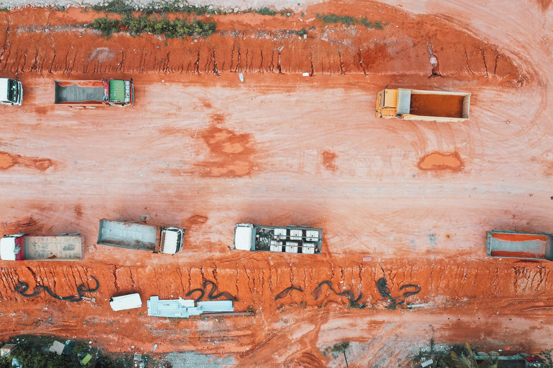 Aerial view of trucks on a construction site with orange soil and earthworks.