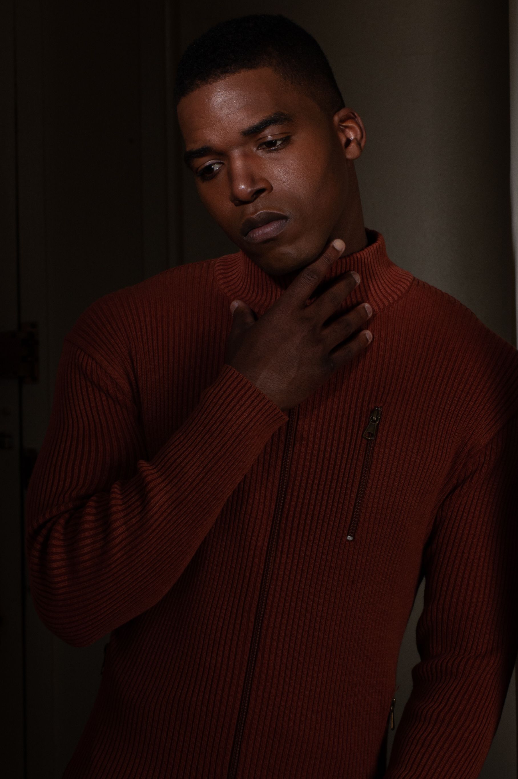 Portrait of a man in a brown knit sweater, looking thoughtful against a dark background.