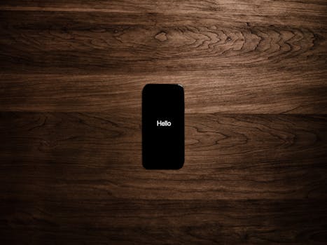 A smartphone displays 'Hello' against a dark wooden background, offering a sleek tech aesthetic.
