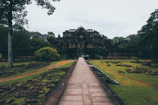 Historic Baphuon Temple at Angkor, Cambodia, amidst lush greenery and ancient ruins.