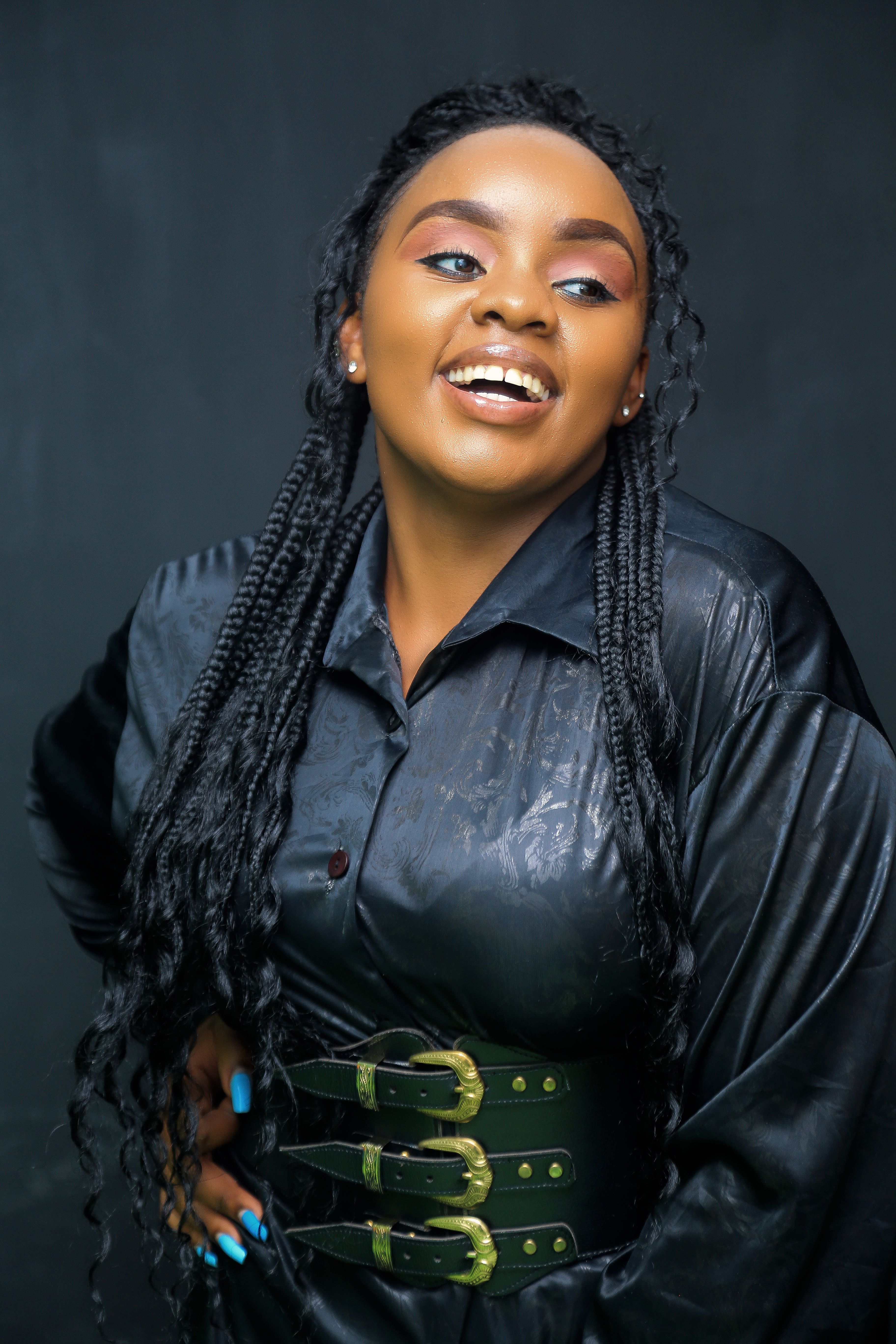 Stylish portrait of a smiling black woman in a studio setting wearing black attire and long braids.