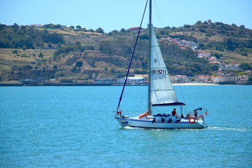 Free A sailboat gliding through clear blue waters with a scenic hillside in the background, perfect for travel or leisure themes. Stock Photo