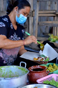 An Asian woman in Bali, Indonesia, prepares a traditional dish at a street market, showcasing local cuisine.
