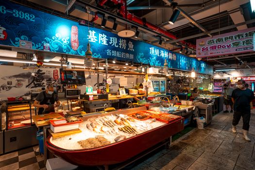 A bustling indoor fish market with a vibrant display of fresh seafood and people shopping.