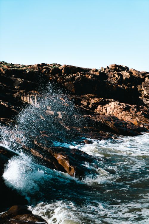 Free Captivating view of ocean waves crashing against rocky coastline under a clear blue sky. Stock Photo
