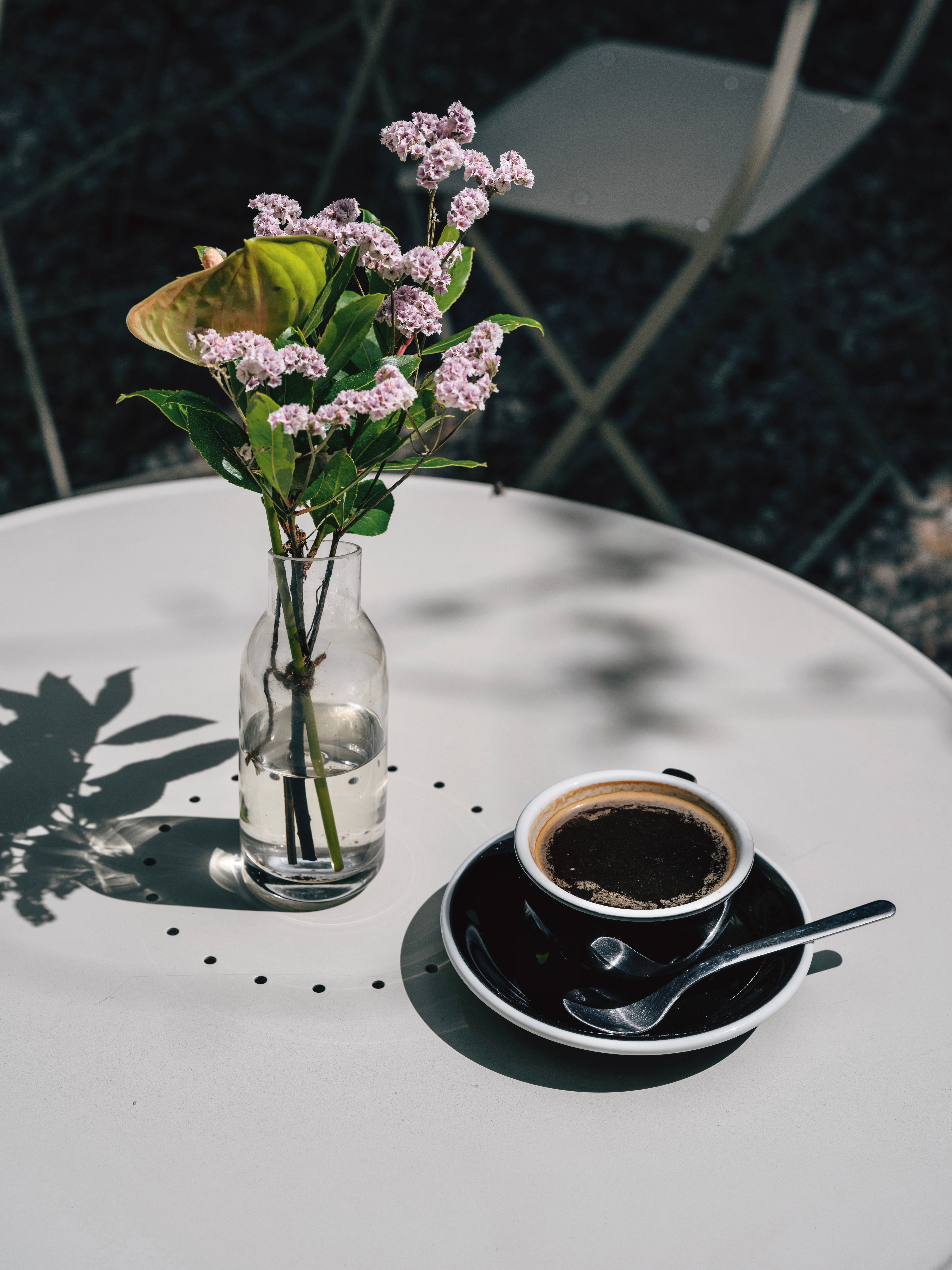 A tranquil café setting featuring a cup of coffee and a vase of flowers on a sunny table.