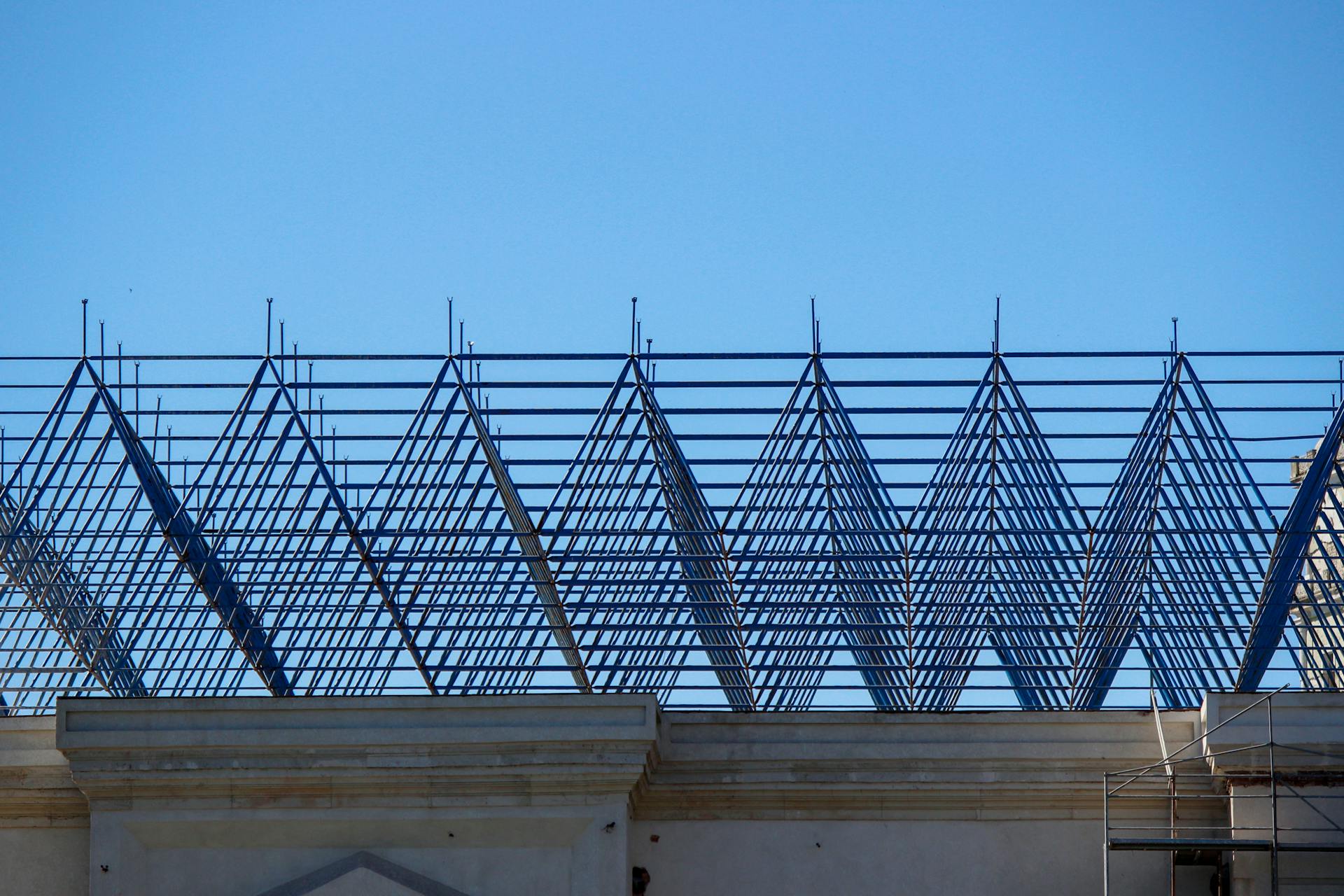 A geometric steel frame of a roof under construction on a building, set against a clear blue sky.