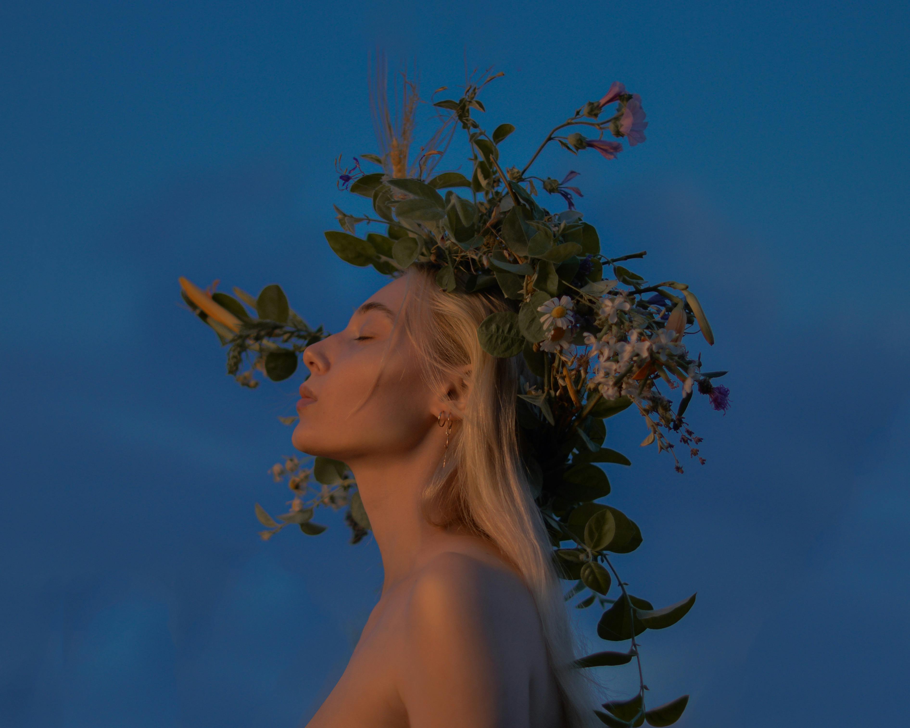 A serene portrait of a young woman adorned with a natural floral wreath under a twilight sky.