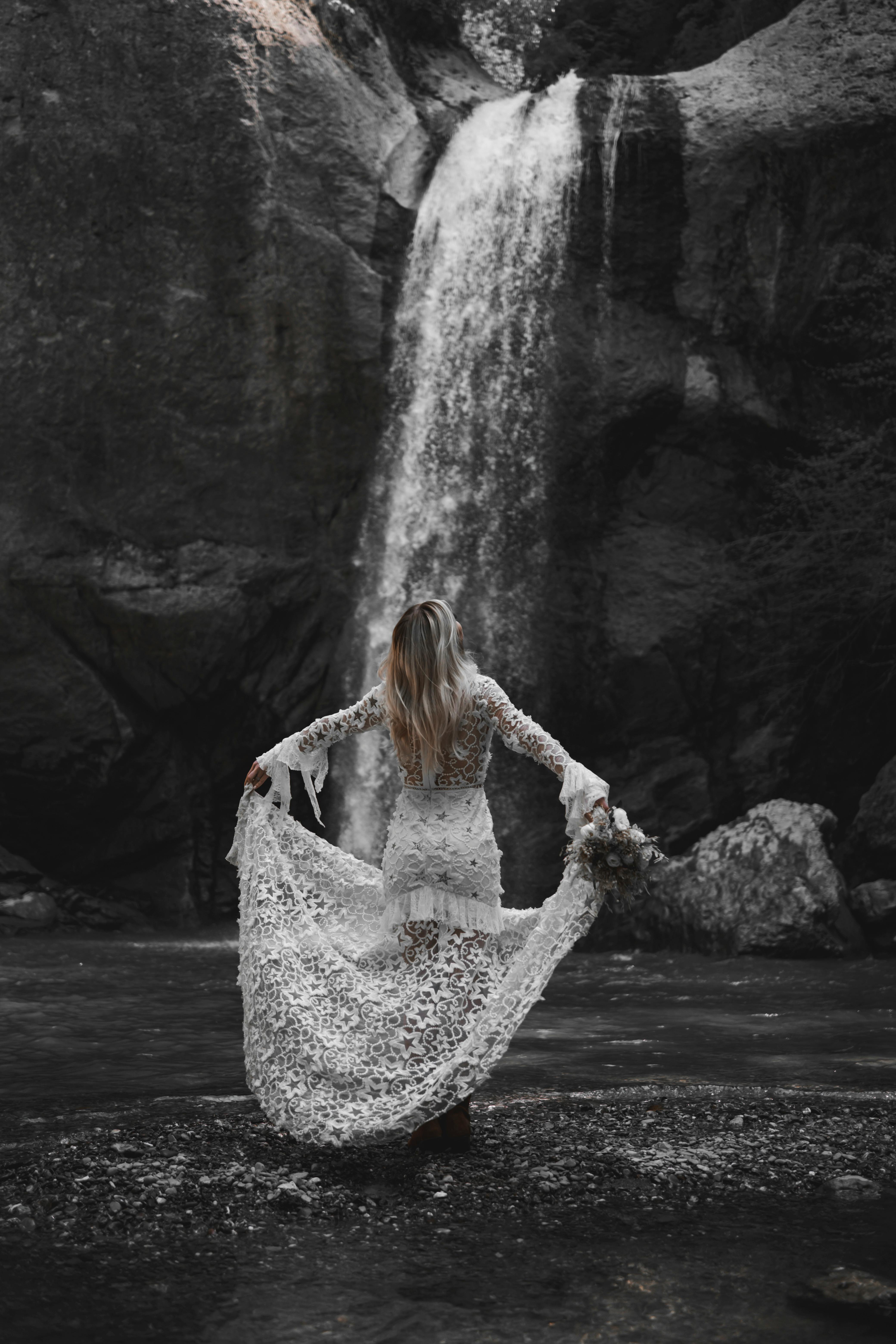 Woman in a Wedding Dress Standing by a Waterfall  Free Stock Photo