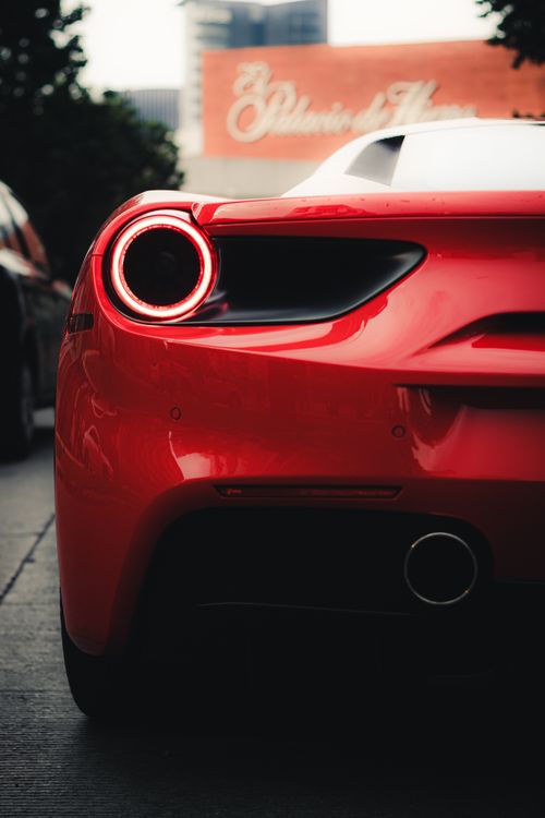 Free Detailed back view of a red supercar showcasing its sleek design and tail lights in an urban environment. Stock Photo