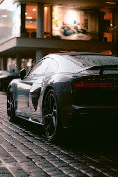 Sleek black luxury car glistening under city lights, captured on a rainy street for a dramatic effect.
