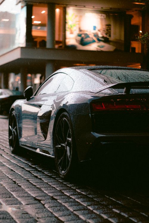 Free Sleek black luxury car glistening under city lights, captured on a rainy street for a dramatic effect. Stock Photo