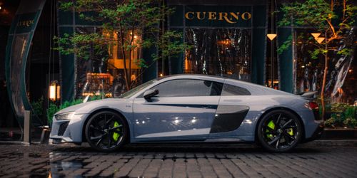 Free Side view of a modern sports car parked by a stylish outdoor restaurant at night. Stock Photo