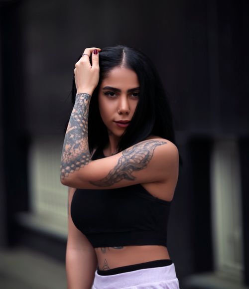 Free Stylish woman in crop top showcasing arm tattoos in an urban setting. Stock Photo