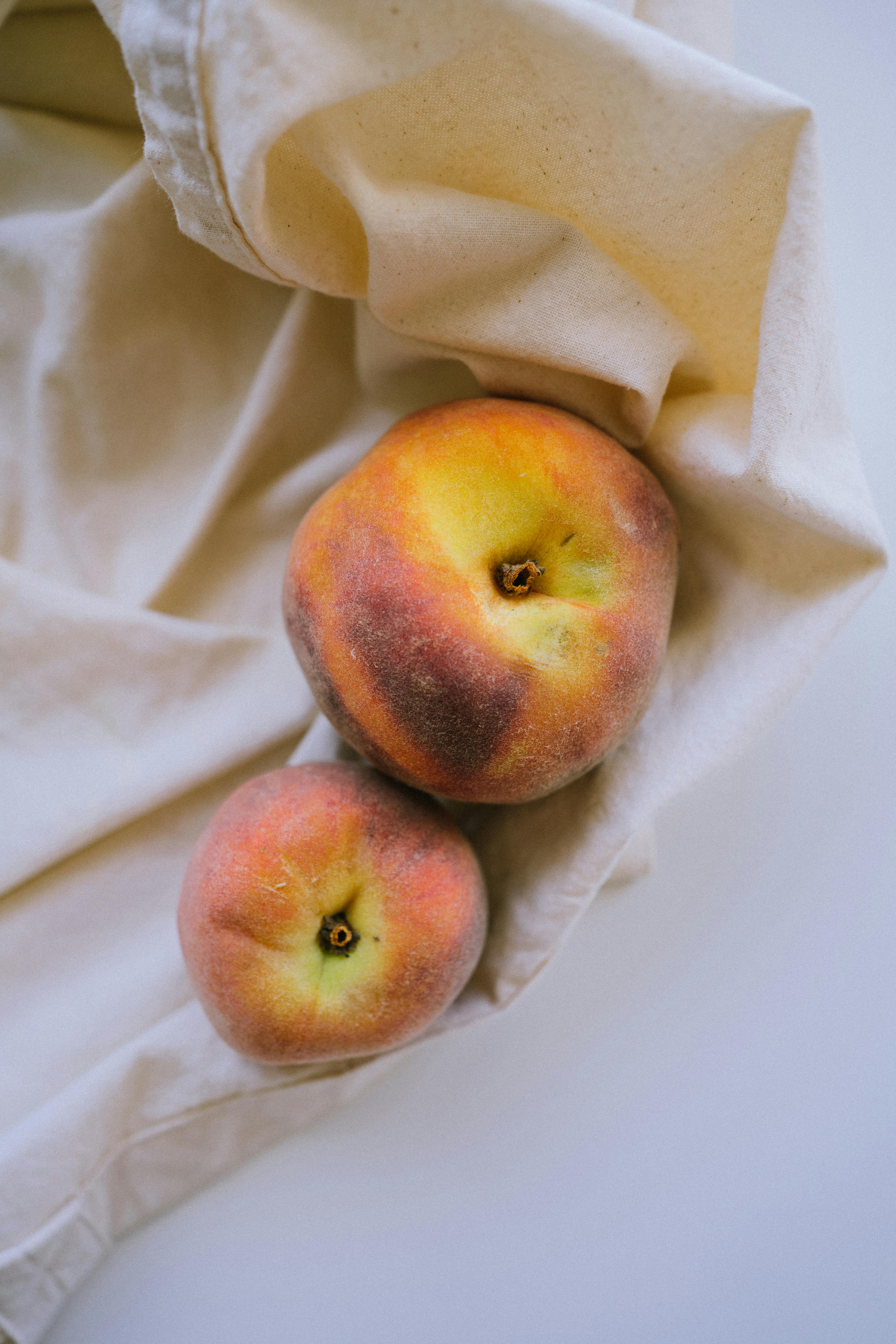 A close-up of fresh peaches resting on soft white fabric, highlighting their natural texture and color.