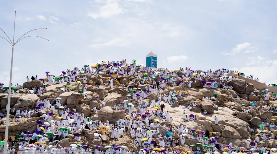 Pilgrims in white sheltering under umbrellas on the rocks of Jabal al-Rahmah at Arafat in the midday sun