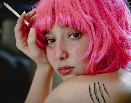 Artistic portrait of a woman with vibrant pink hair holding a cigarette, showcasing individuality and bold style.