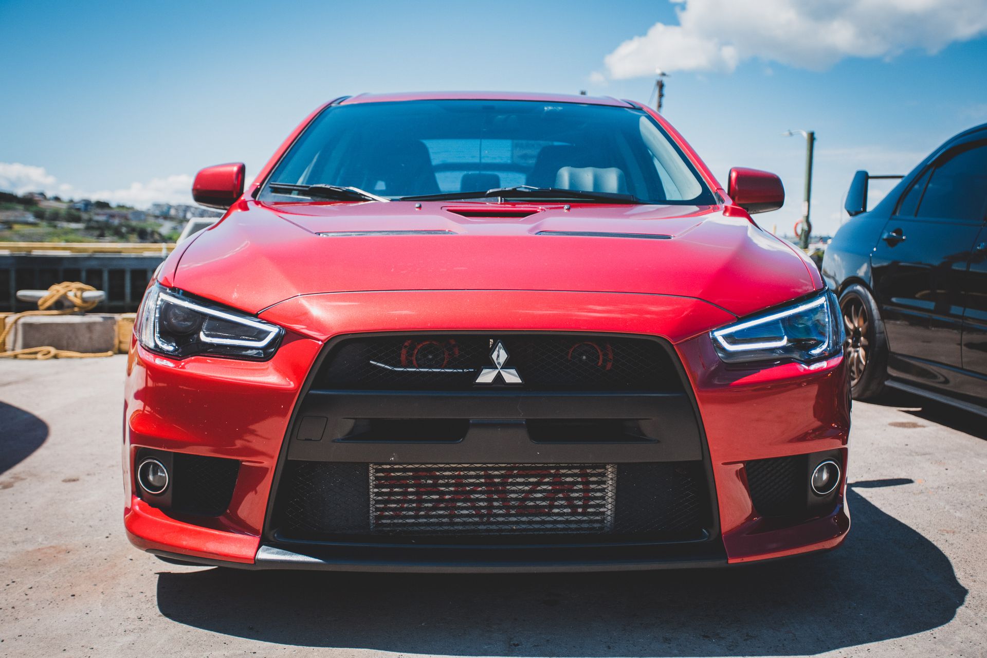 Front view of a red Mitsubishi Lancer Evolution parked outdoors under a blue sky.