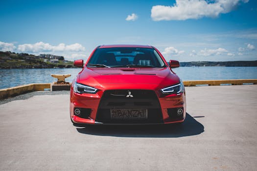 A vibrant red Mitsubishi Lancer parked on a pier with a scenic sea backdrop.