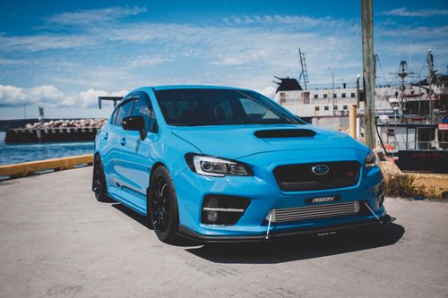 Free A sleek blue sports sedan parked at a seaside port under clear skies. Stock Photo