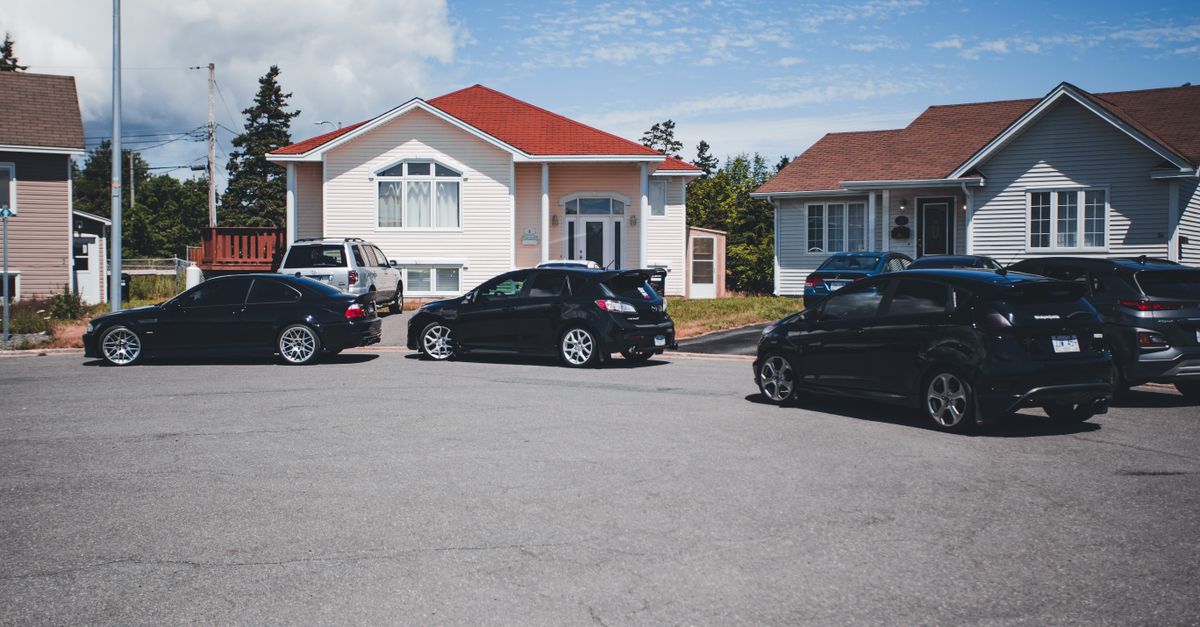 A quiet suburban street with parked cars in front of modern houses under a clear blue sky.